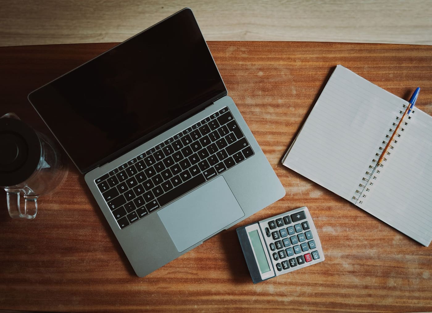 Top view of a desk with an open laptop, a small calculator and a notepad