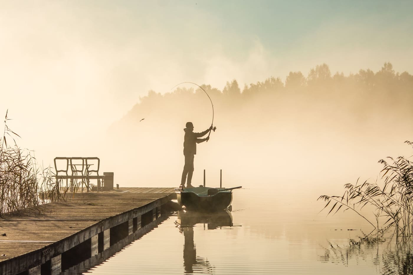 A lone fisherman casting a line from a wooden dock on a misty lake