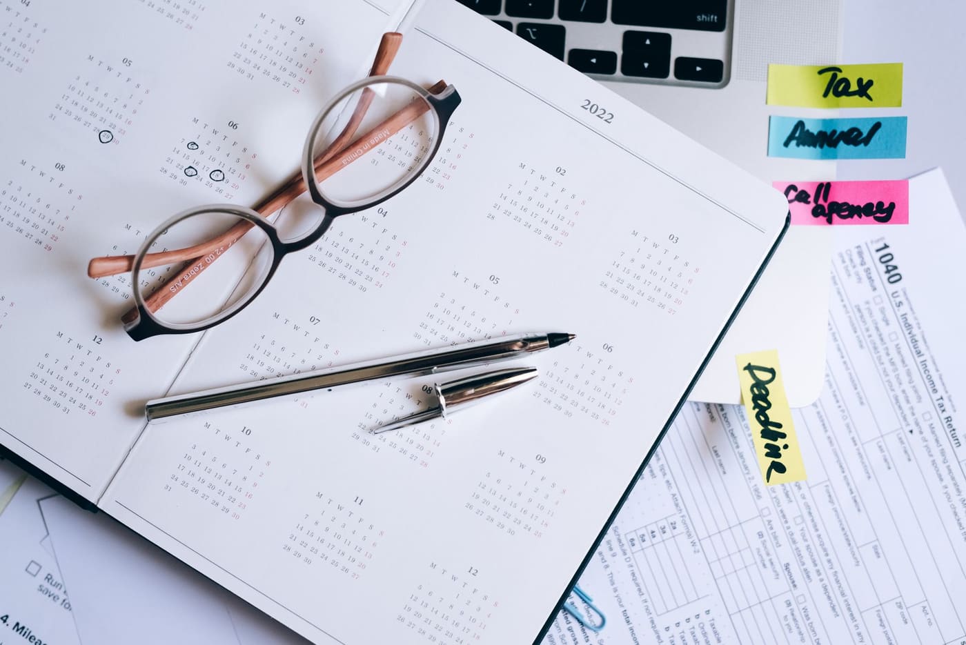 Reading glasses and a pen resting on a planner beside tax documents