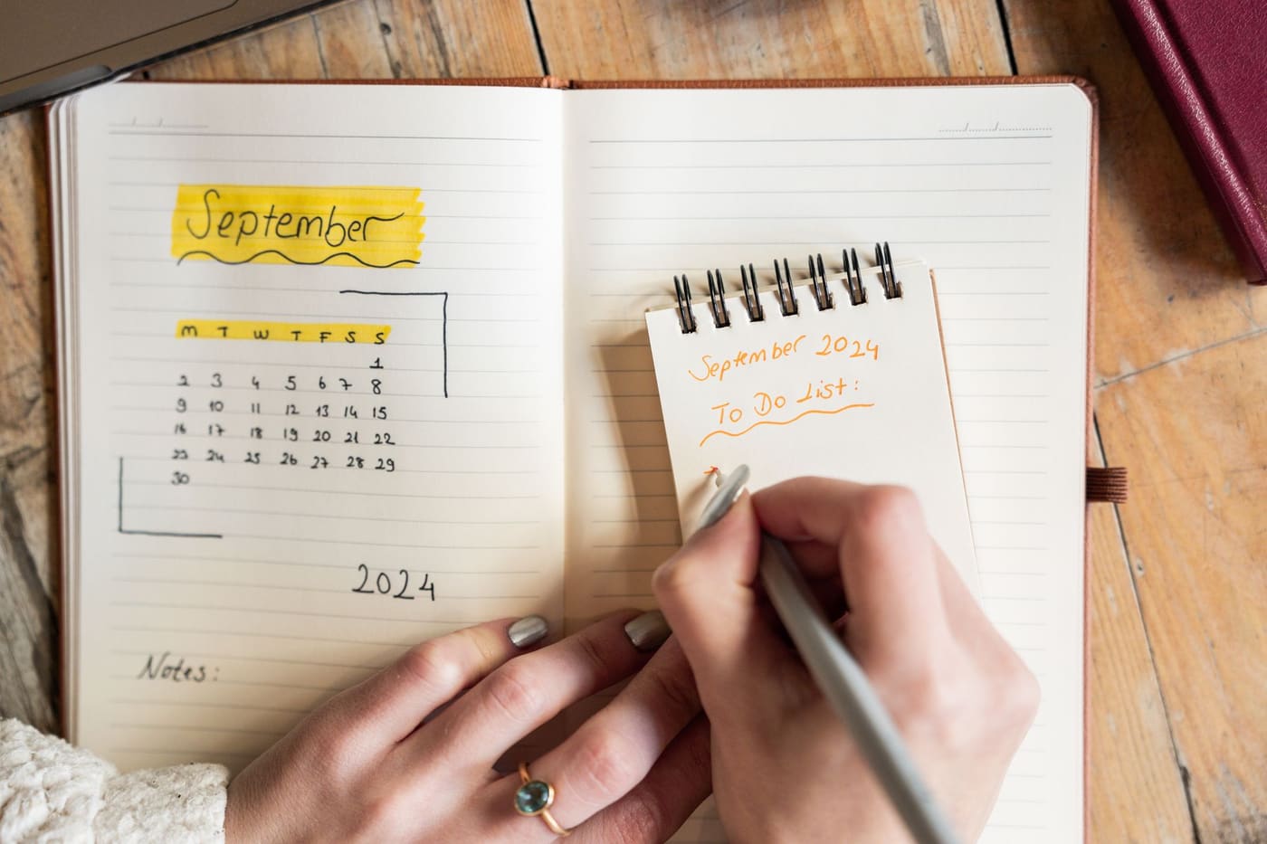 Hands writing a to-do list in an open planner notebook on a wooden desk
