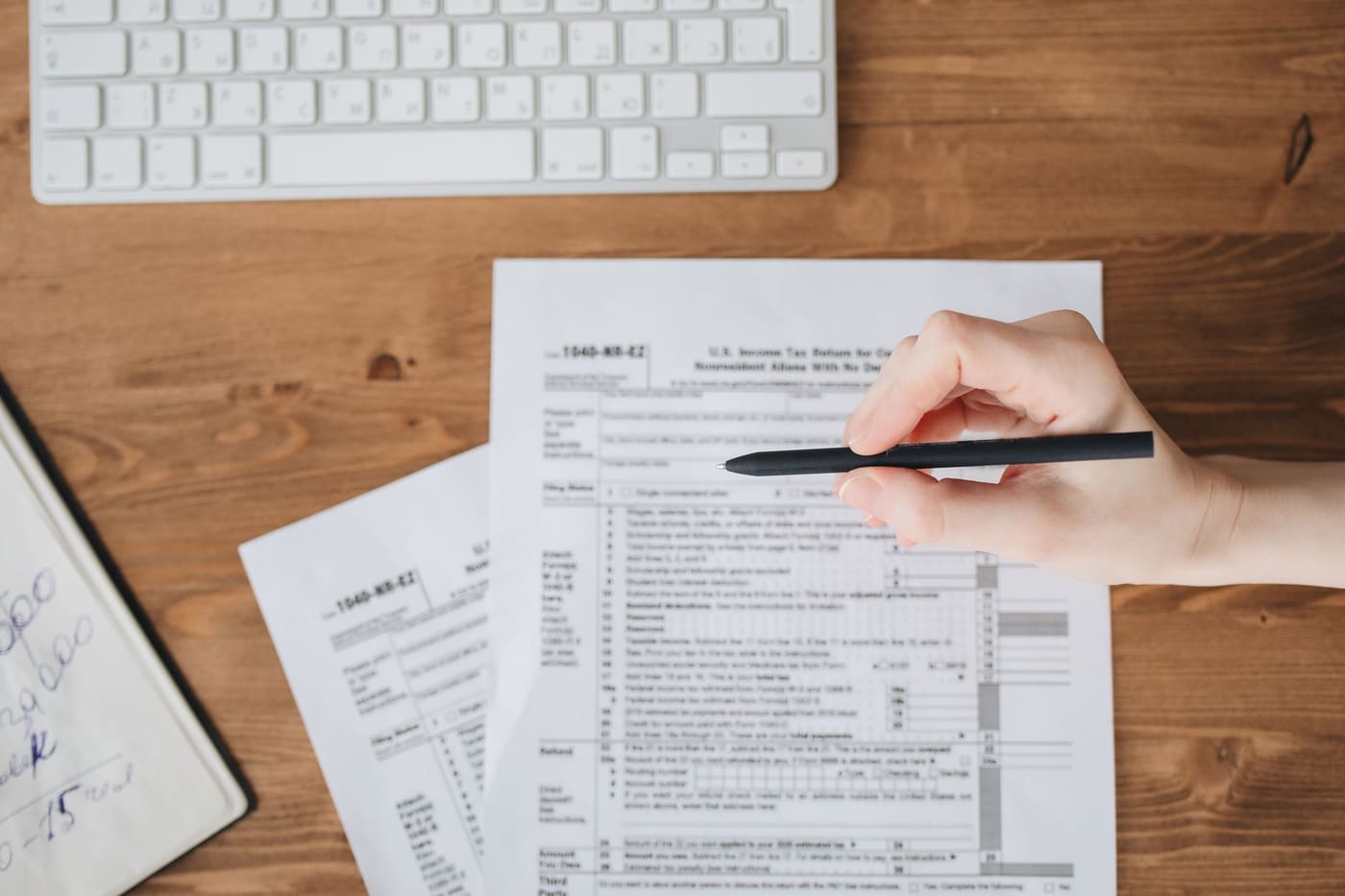 A hand holding a pen over a US tax form on a wooden table