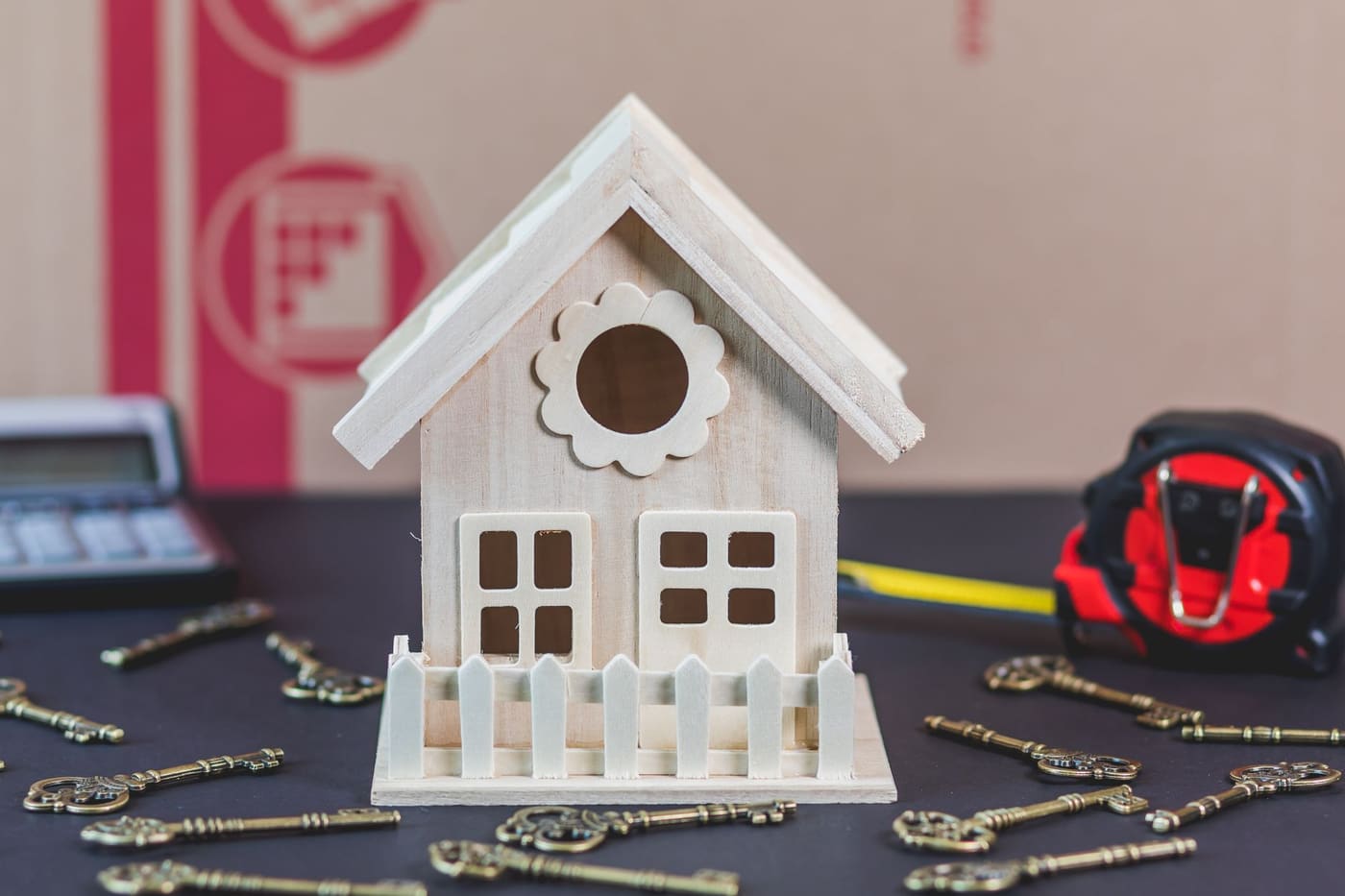 A small white wooden model house on a table beside a scatter of old-style keys